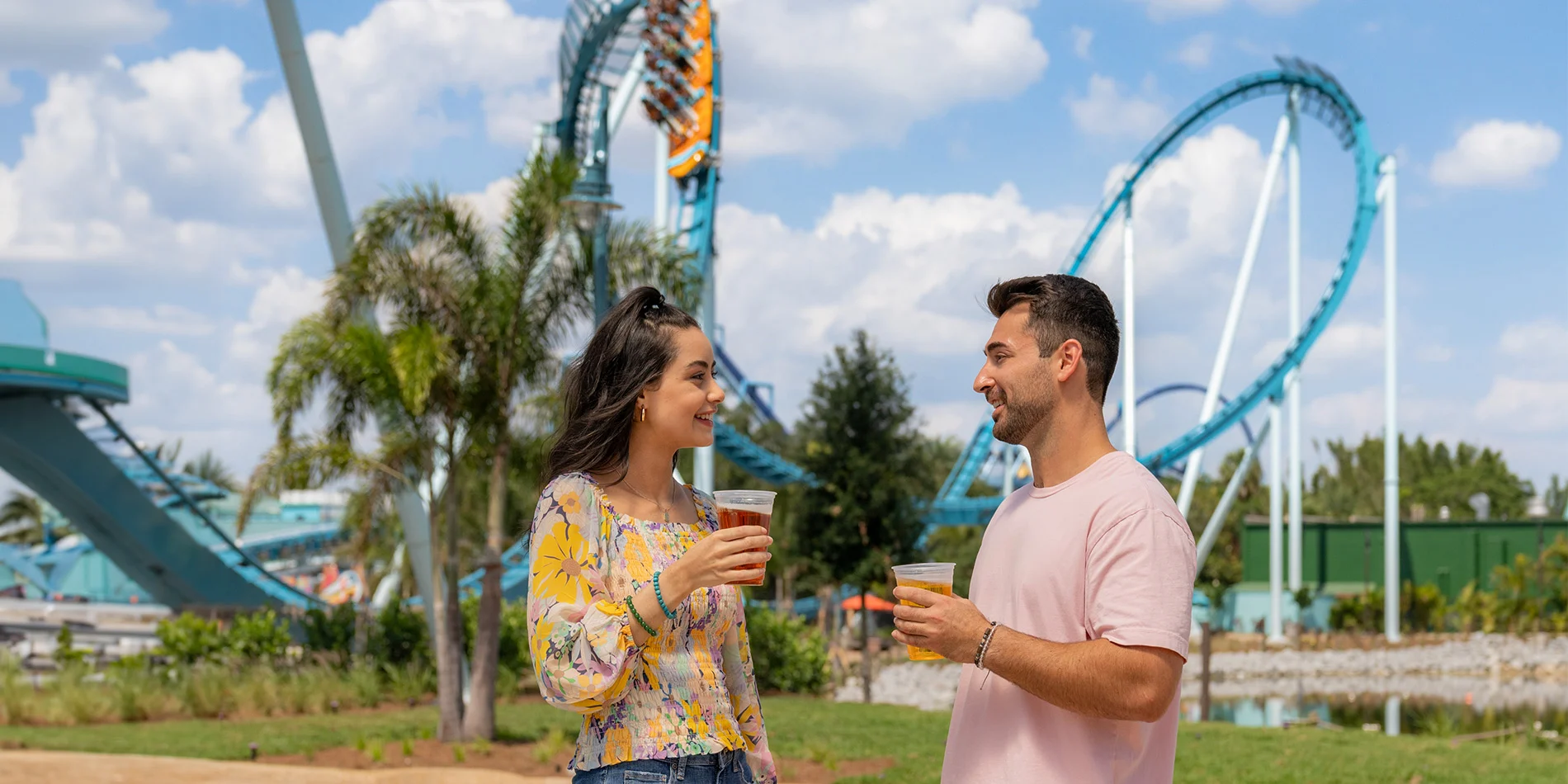 two people drinking beer in front of a rollercoaster